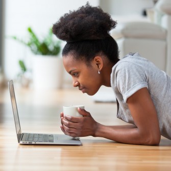 Woman on floor with cup looking at laptop
